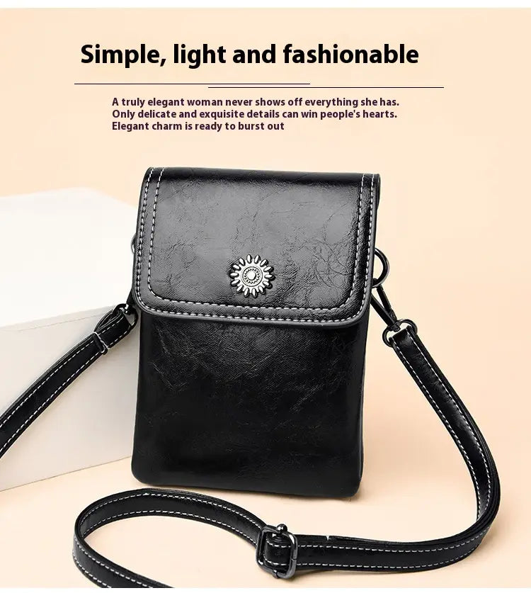 Schwarze Ledertasche aus Kunstleder mit floralen und Sonnenstrahl-Details, Umhängetasche für das Telefon, mit silbernem Sonnenstrahl-Verschluss und weißer Ziernaht entlang der Kanten.