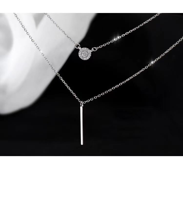 A delicate double layer silver necklace featuring a pave-set round zircon pendant and a minimalist vertical bar pendant.
