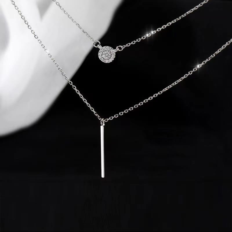 A delicate double layer silver necklace featuring a round pave zircon pendant and a sleek vertical bar charm.