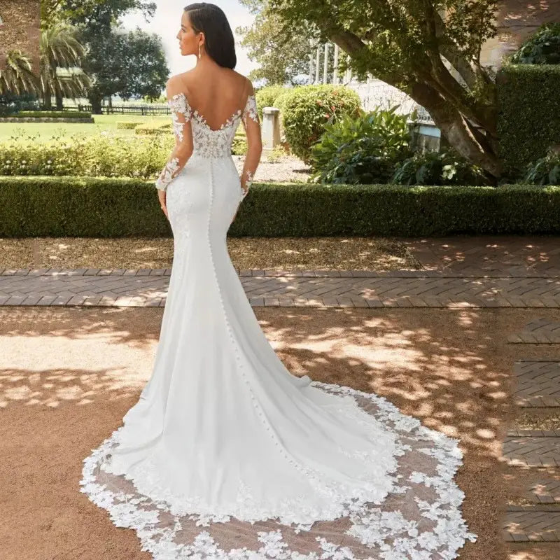 Une robe de mariée sirène en dentelle à épaules dénudées blanche, avec des détails de dentelle complexes au dos et sur les manches, ainsi qu’une silhouette ajustée qui se prolonge en une traîne élégante, présentée vue de dos.