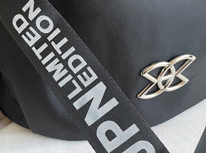 black fabric strap with white limited edition text and a silver metallic logo emblem on the waterproof large capacity nylon travel backpack with PU leather trim