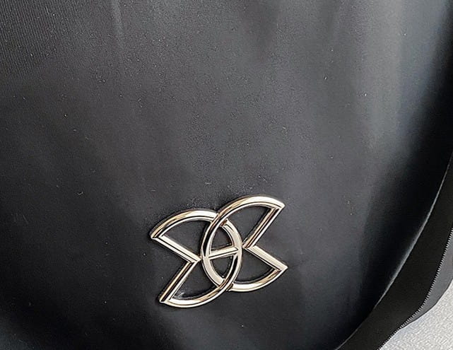 silver metallic logo emblem on black nylon fabric with pu leather trim of waterproof large capacity travel backpack