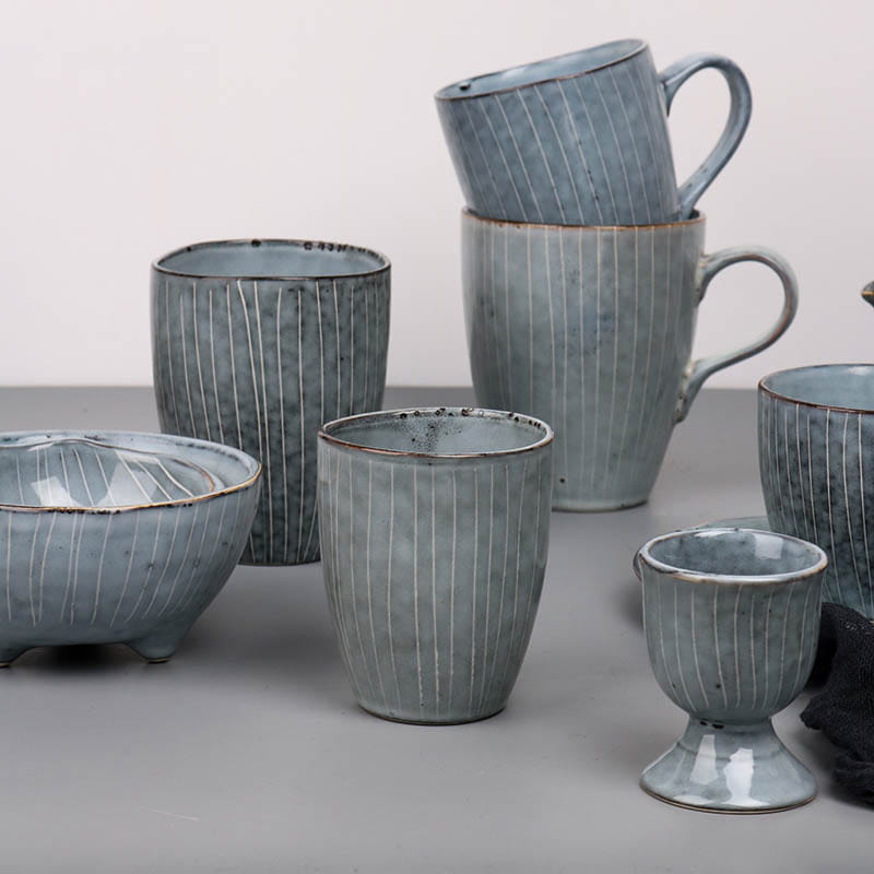 Set of handcrafted ceramic mugs and bowls in muted blue-gray glaze with subtle vertical striations from the ceramic dinnerware set retro ribbed plates and bowls.