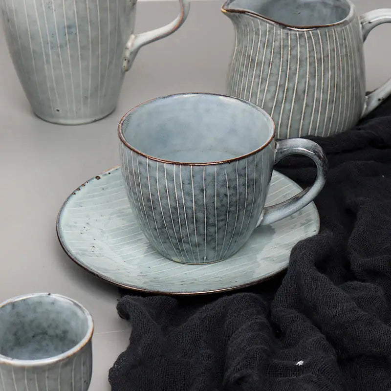 A textured sage green ceramic mug with vertical ridges and a rustic brown rim resting on its matching saucer from the ceramic dinnerware set retro ribbed plates and bowls.