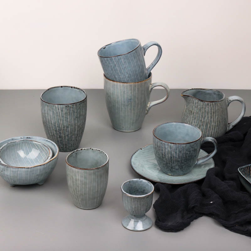 Set of handcrafted ceramic dinnerware including retro ribbed plates and bowls in muted blue-gray glaze with subtle vertical striations and rustic uneven rims.