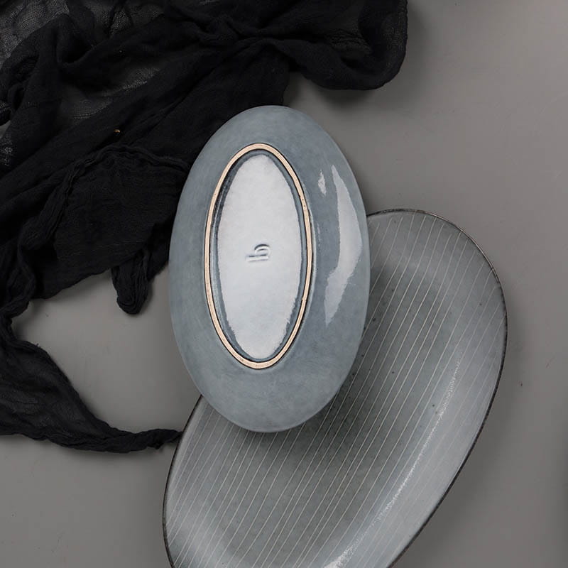 A sleek light gray ceramic oval dish with a subtle glossy finish and delicate gold rim part of a ceramic dinnerware set retro ribbed plates and bowls.