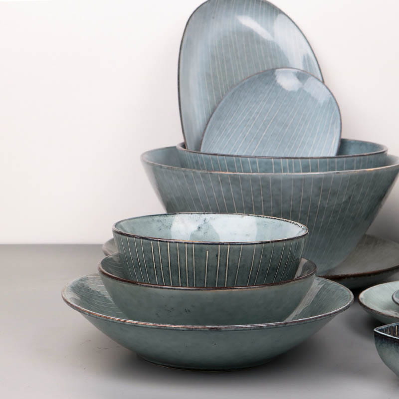 Set of ceramic dinnerware with a matte blue glaze and subtle vertical ridges featuring retro ribbed plates and bowls.