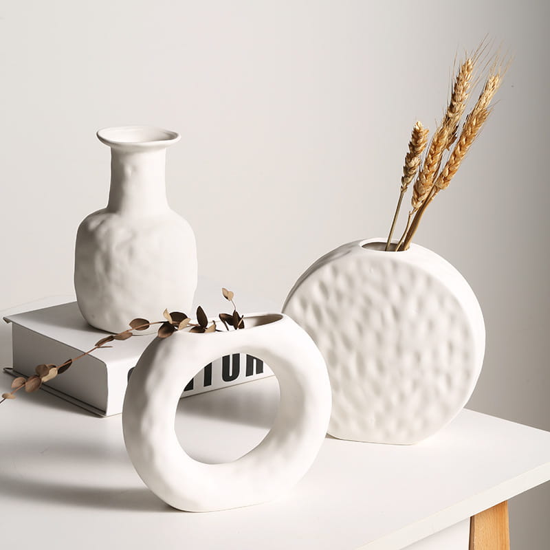 White ceramic vases with a textured hammered finish and minimalist geometric shapes for Scandinavian interior decoration.