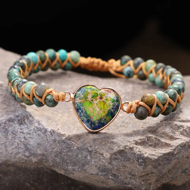 Handmade woven heart stone pendant bracelet featuring a heart-shaped turquoise and green stone set in a gold-toned frame within a braided bracelet of matching turquoise beads.