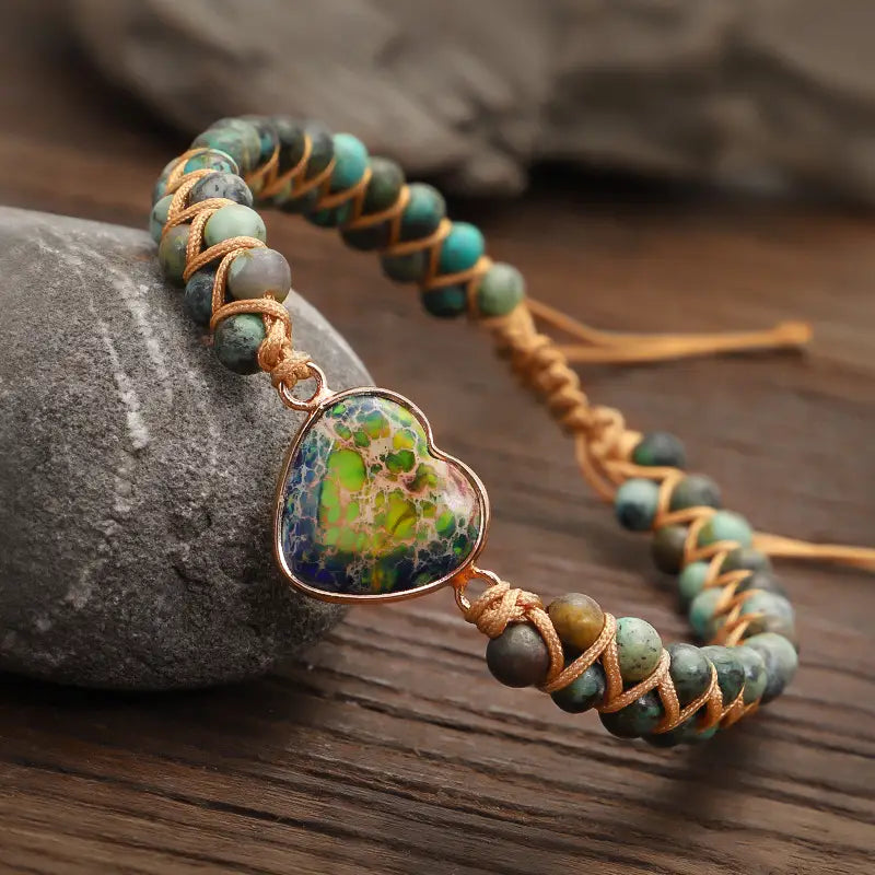 Handmade woven heart stone pendant bracelet featuring turquoise and green stone beads woven with golden thread and a rose gold heart-shaped pendant with swirling blue-green patterns.