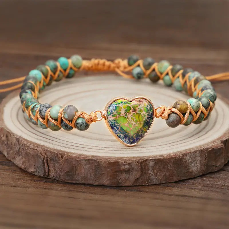 Handmade woven heart stone pendant bracelet featuring a heart-shaped pendant with a vibrant marbled green and blue pattern set in gold-tone metal on a braided turquoise bead bracelet.