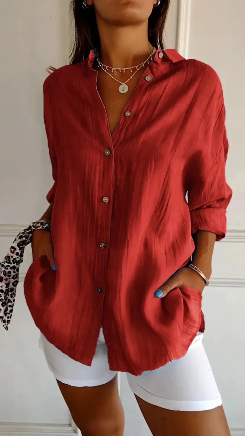 A rust-red women’s relaxed pleated button-up shirt made of subtle textured fabric with rolled sleeves.