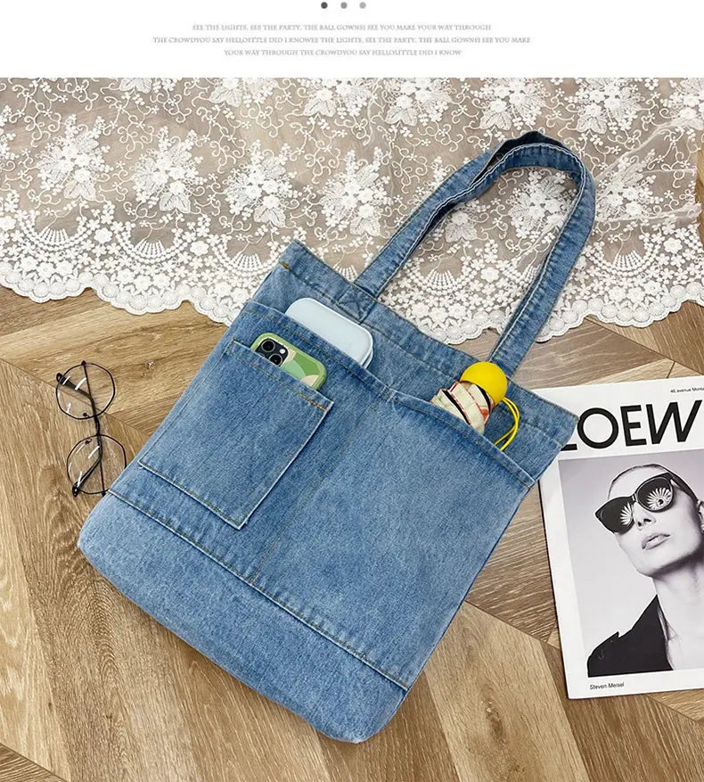 Blue denim tote bag with two front pockets, embroidered slogan, and soft top handle.