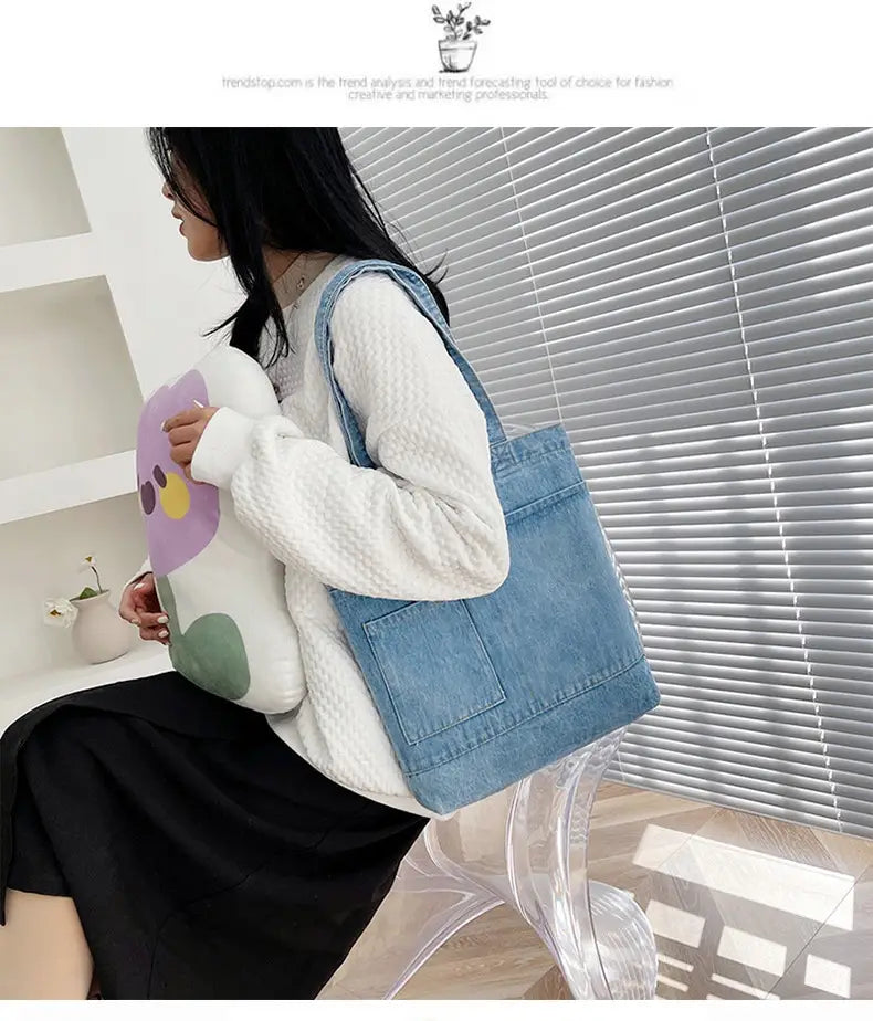 Blue denim tote bag with embroidered slogan, front pocket, soft handle, and shoulder strap.