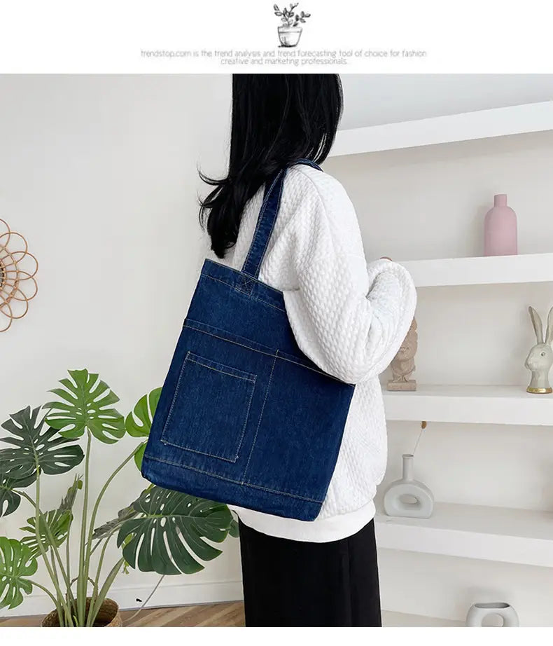 Blue denim tote bag with front pocket, embroidered slogan, and soft sturdy handles made from durable denim material.