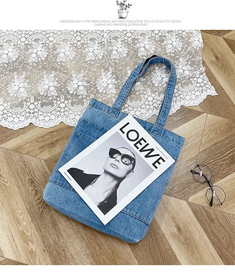 Blue denim embroidered tote bag with soft handles and a front pocket featuring a loewe magazine resting on top.