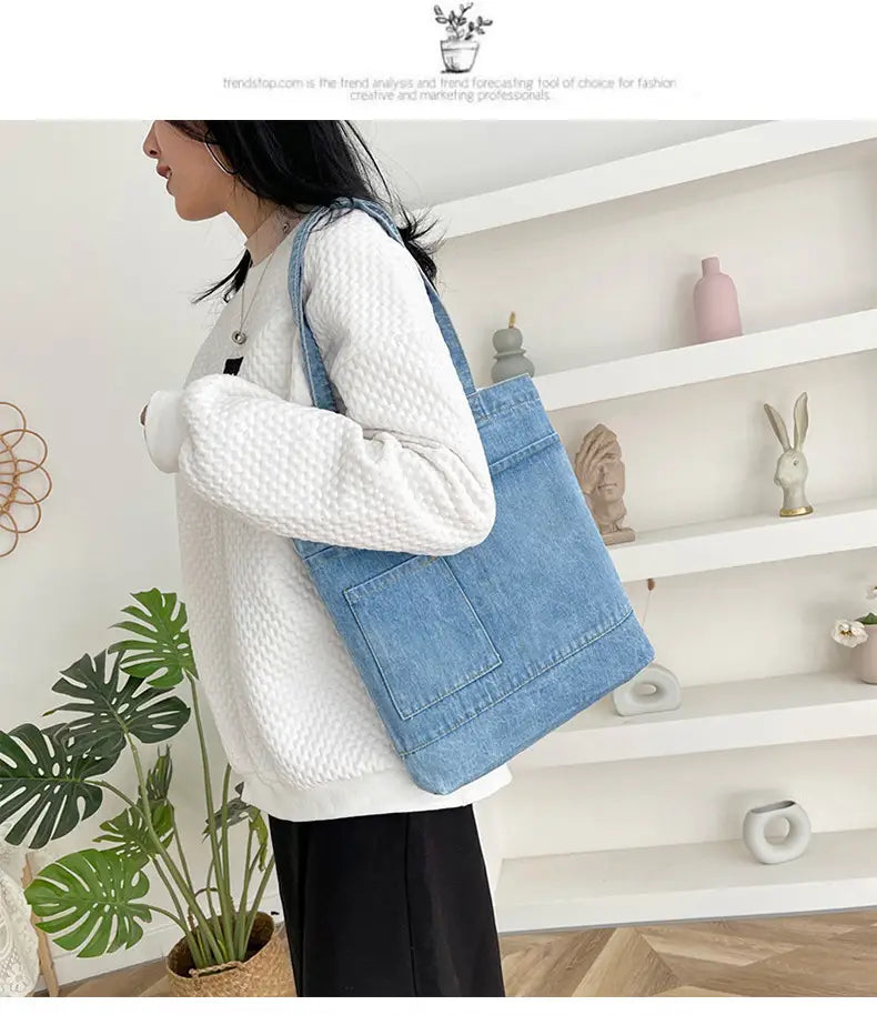 Light blue embroidered denim tote bag with a single shoulder strap front pocket and a soft handle featuring a slogan.