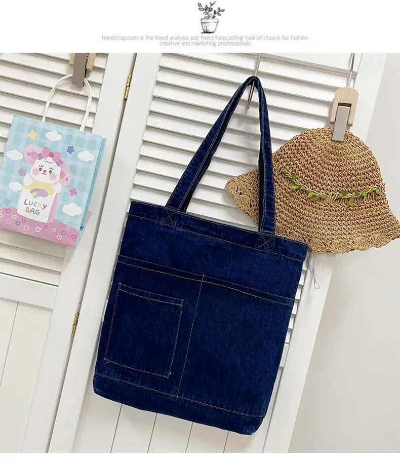 Deep blue denim tote bag with embroidered slogan, front pocket, and soft sturdy handles.