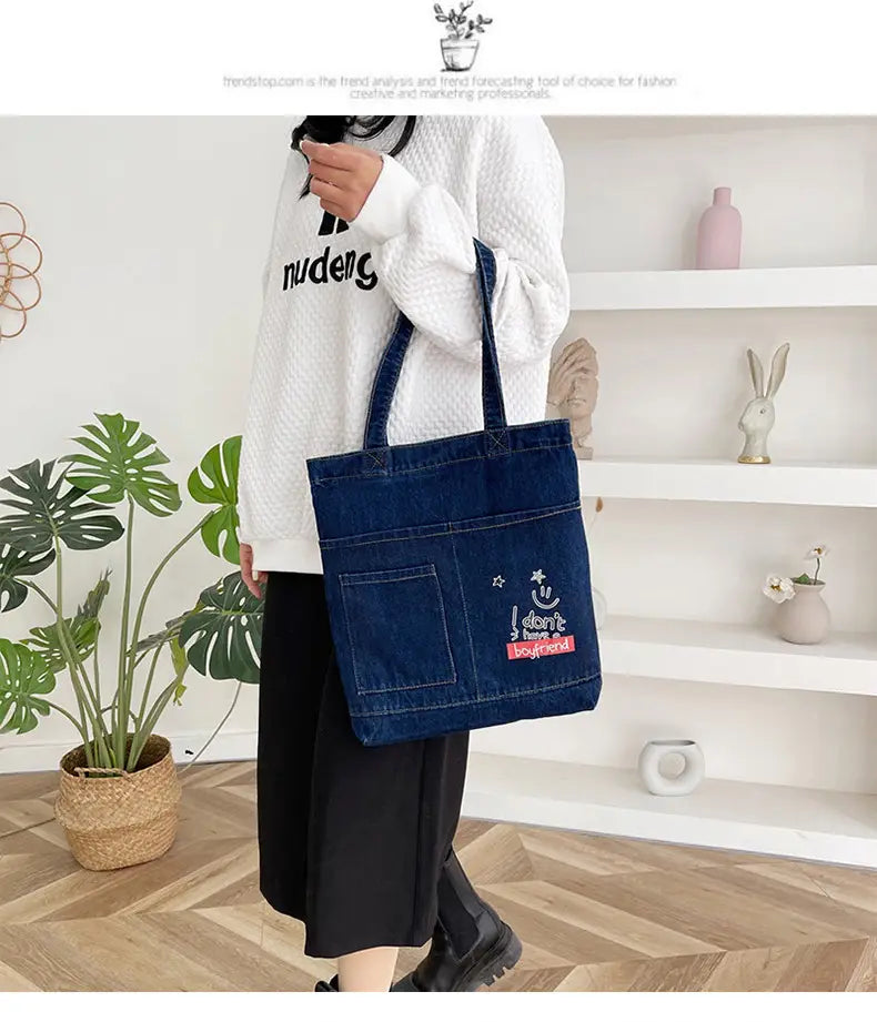 Blue denim tote bag with soft handle featuring a smiling face and i don t have boyfriend text patch embroidered on the front.