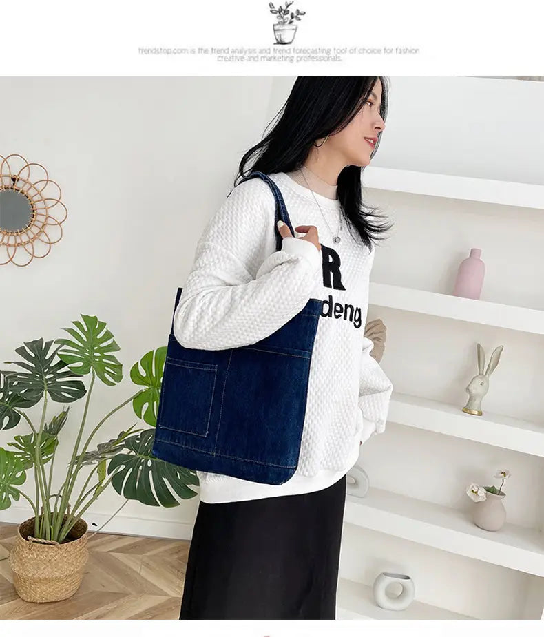 Blue denim embroidered tote bag with front pocket and shoulder strap featuring a soft handle and slogan design.