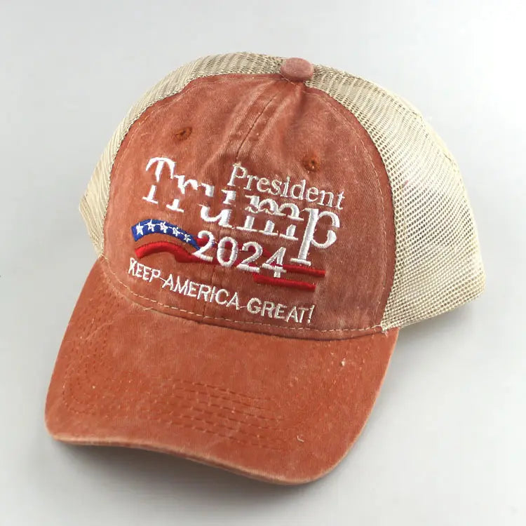 A distressed orange trucker hat with a beige mesh back featuring embroidered white text reading president trump 2024 and keep america great above a red white and blue banner design, labeled Trump 2024 embroidered trucker hat.