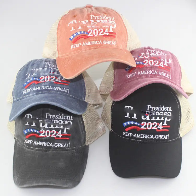 A collection of distressed trucker hats in faded orange navy blue and black with beige mesh backs featuring embroidered president trump 2024 text and a red white and blue banner design in the Trump 2024 embroidered trucker hat product.