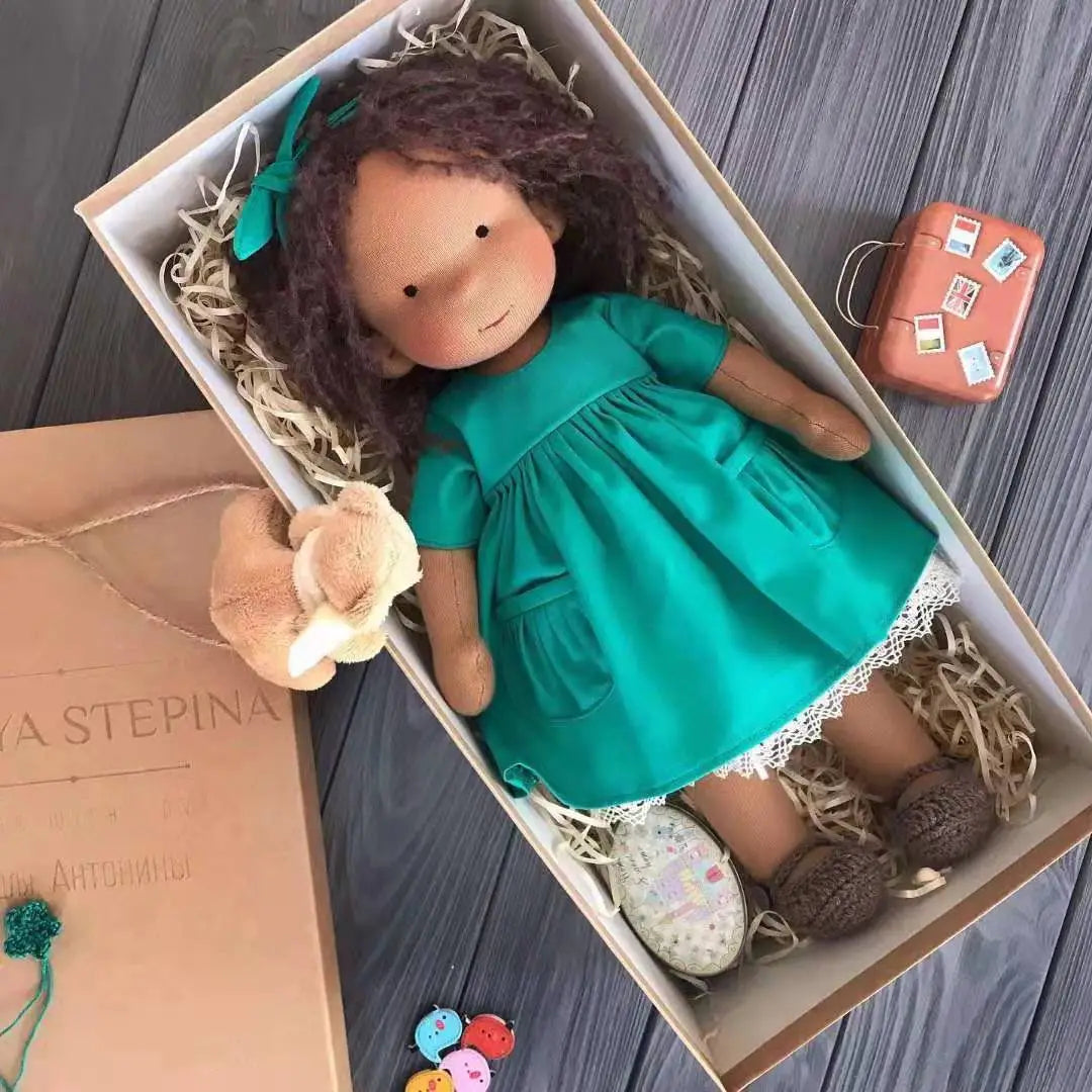 Eine handgemachte Plüschpuppe mit goldenen lockigen braunen Haaren, gekleidet in ein türkisfarbenes Kleid, gebettet in eine strohgefütterte Schachtel.