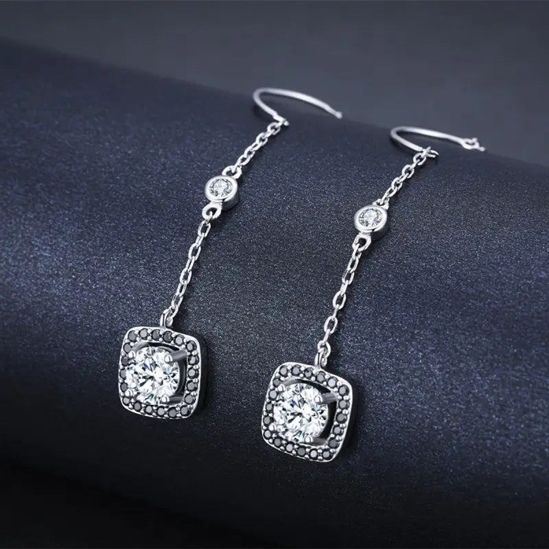 Silver plated zircon square drop earrings featuring a central round clear stone surrounded by smaller black stones in a square setting connected to the ear wire by a delicate chain.