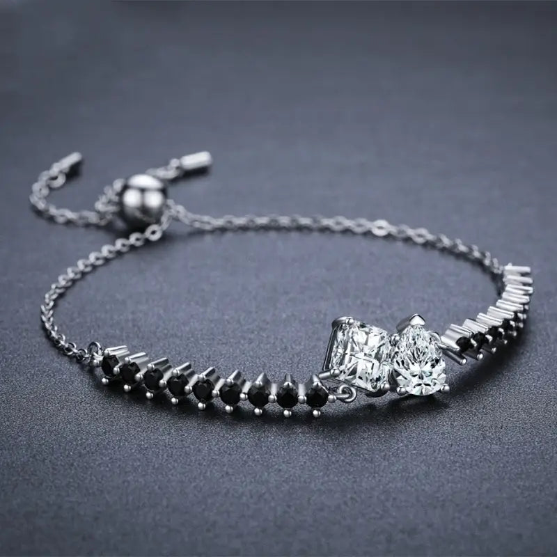 Sterling silver bracelet featuring a delicate chain with two clear-cut gemstones and a row of black accent stones accented by small spherical beads in a zircon heart pendant and bracelet set.
