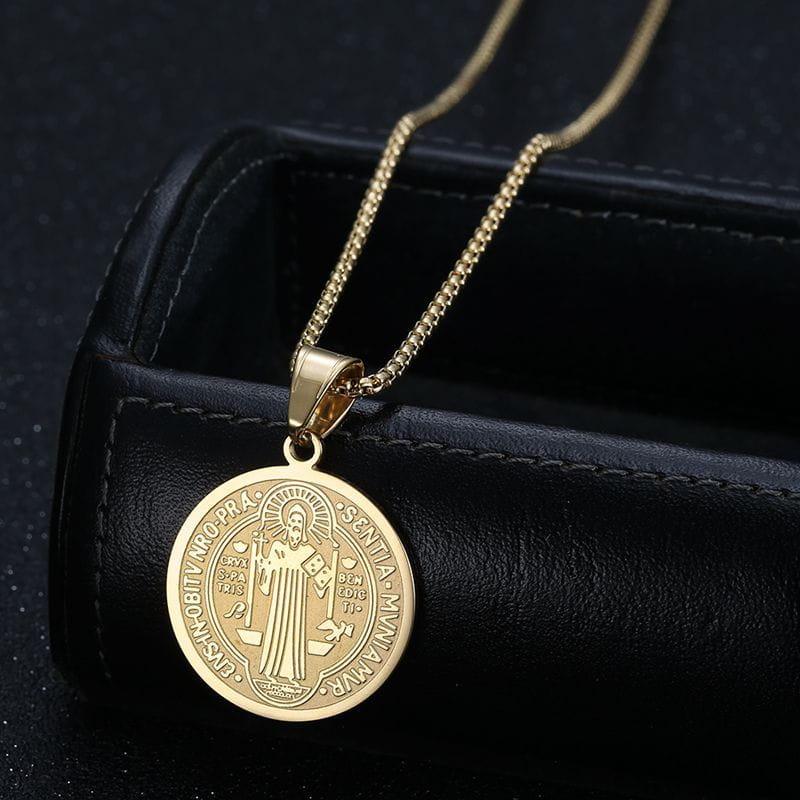 Gold-toned stainless steel saint benedict medal pendant necklace with an engraved religious figure and latin inscription on a matching chain.