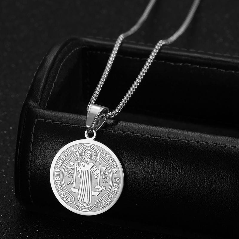 Stainless steel saint benedict medal pendant necklace in silver featuring an engraved religious figure and latin inscription on a fine chain.