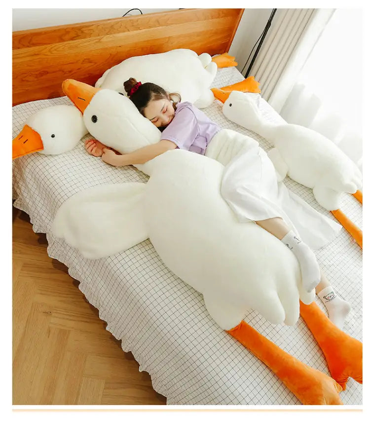 Un grand coussin-peluche oie blanche en forme de corps, avec un bec et des pattes orange, conçu pour le confort et les câlins.