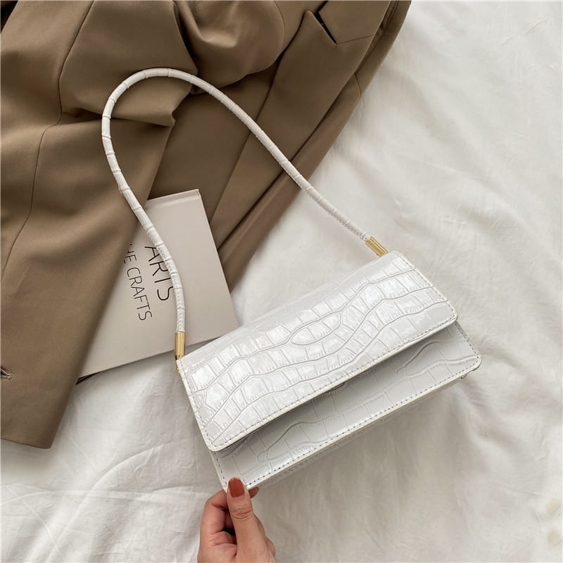 White crocodile textured crossbody bag with gold tone hardware and slender matching strap made of high end pu material designed as a clutch for underarm use.