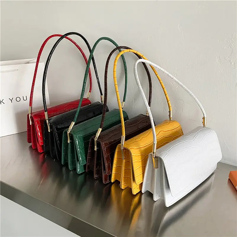 A collection of high-end pu clutch crocodile pattern underarm bags in red black green brown yellow and white with curved handles.