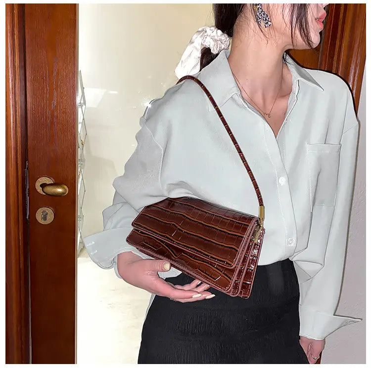 Brown crocodile-textured underarm bag with a slender shoulder strap made of high-end PU material for use as a clutch.