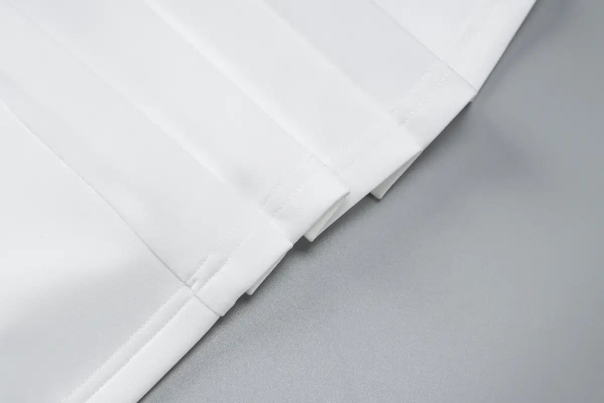 Tissu blanc plissé présentant des plis nets et réguliers, mis en valeur dans une robe mini blazer à manches longues volantées et décolleté plongeant en V