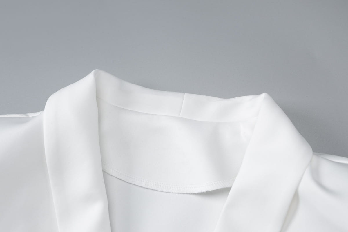 Détail de col en satin blanc sur une robe mini blazer à manches longues et décolleté plongeant en V, avec volants