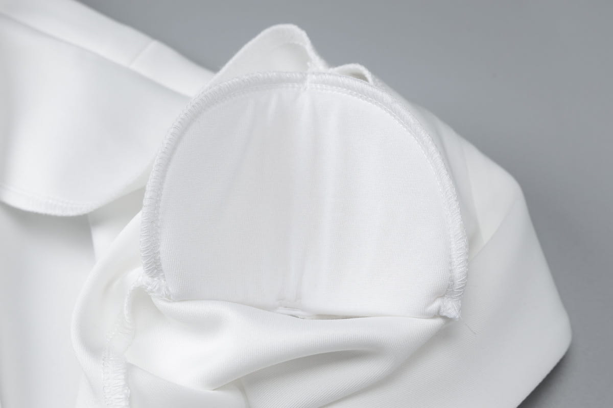 Tissu blanc type satin, fini lisse et brillant, avec des bords cousus avec précision, utilisé pour une robe mini blazer à manches longues et décolleté plongeant en V, avec volants.