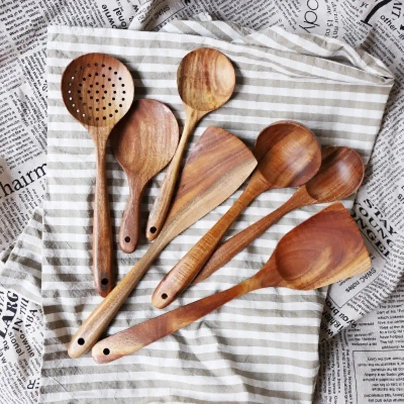 Juego de seis utensilios de cocina de madera de teca artesanal, con vetas naturales y tonos marrón cálido, que incluye una cuchara ranurada para uso en la cocina.