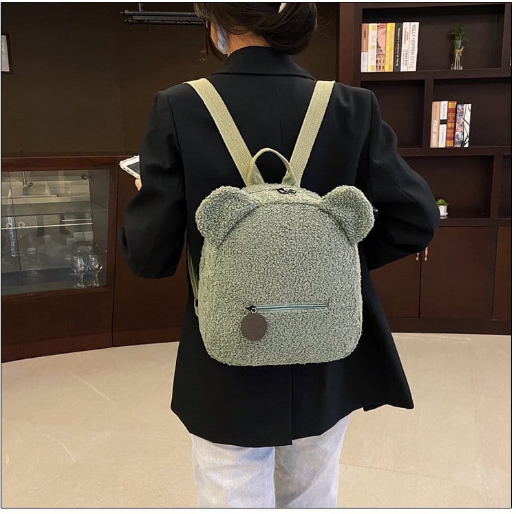 A soft light green teddy bear shaped plush backpack with fuzzy fleece texture and beige straps shown from the back side.