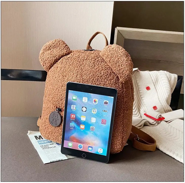 Cute brown teddy bear shaped plush backpack with soft fuzzy fleece texture and rounded ears.