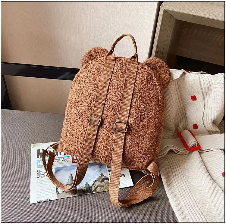 Cute tan bear shaped plush backpack with fuzzy fleece texture and matching leather straps displayed from the back side