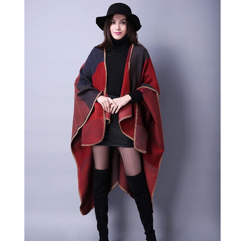 Cape en laine à carreaux surdimensionnée rouge et noire avec des bords finition ton or, présentant des motifs géométriques, conçue comme étole de voyage.
