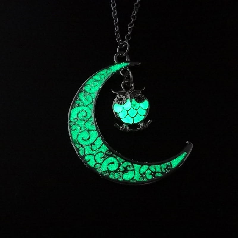 A glowing green crescent moon pendant necklace with intricate swirling patterns and a small owl charm perched on its curve.