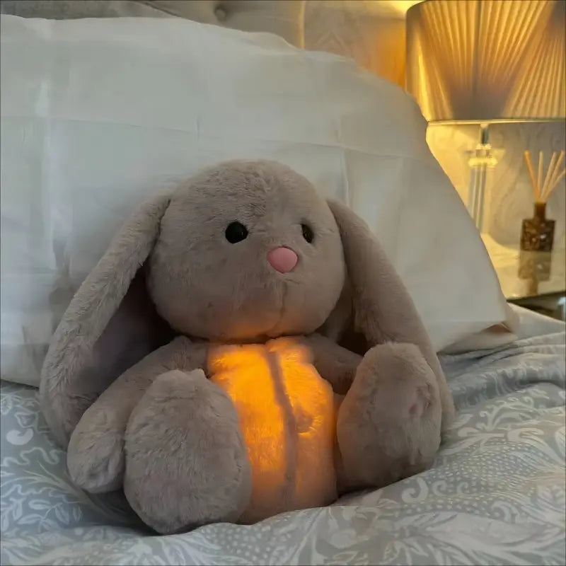 Ein weiches graues Plüschkaninchen, das atmet; beruhigendes Sinnes-Plüschbabyspielzeug mit langen, herabhängenden Ohren, schwarzen Knopfaugen, einer rosafarbenen Nase und einem leuchtend orangefarbenen Licht, das aus seinem Bauch leuchtet.