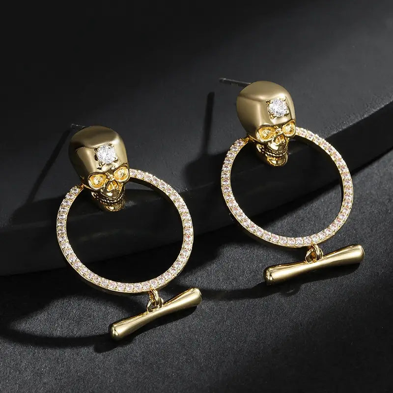 aretes de borla de calavera de oro con una argolla circular dorada engastada con diamantes y un colgante con forma de hueso con acentos de zirconio