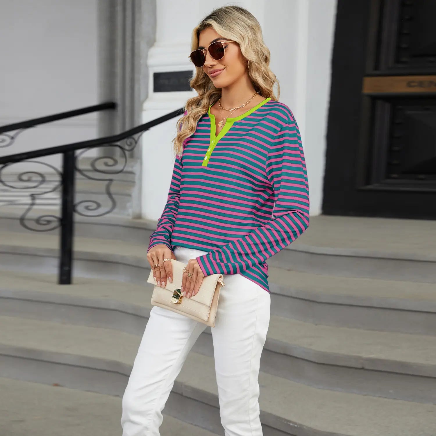 A woman wearing a striped contrast henley long sleeve v neck t shirt with pink and teal horizontal stripes and a neon green v neck collar.