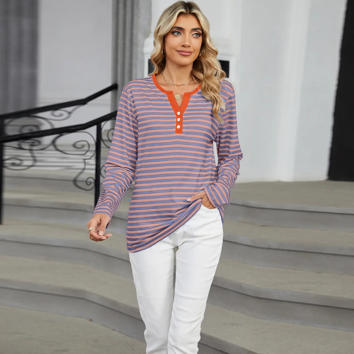 A long-sleeved henley v neck t shirt with horizontal stripes in soft lavender and muted pink featuring a contrasting orange collar and placket with three matching buttons.