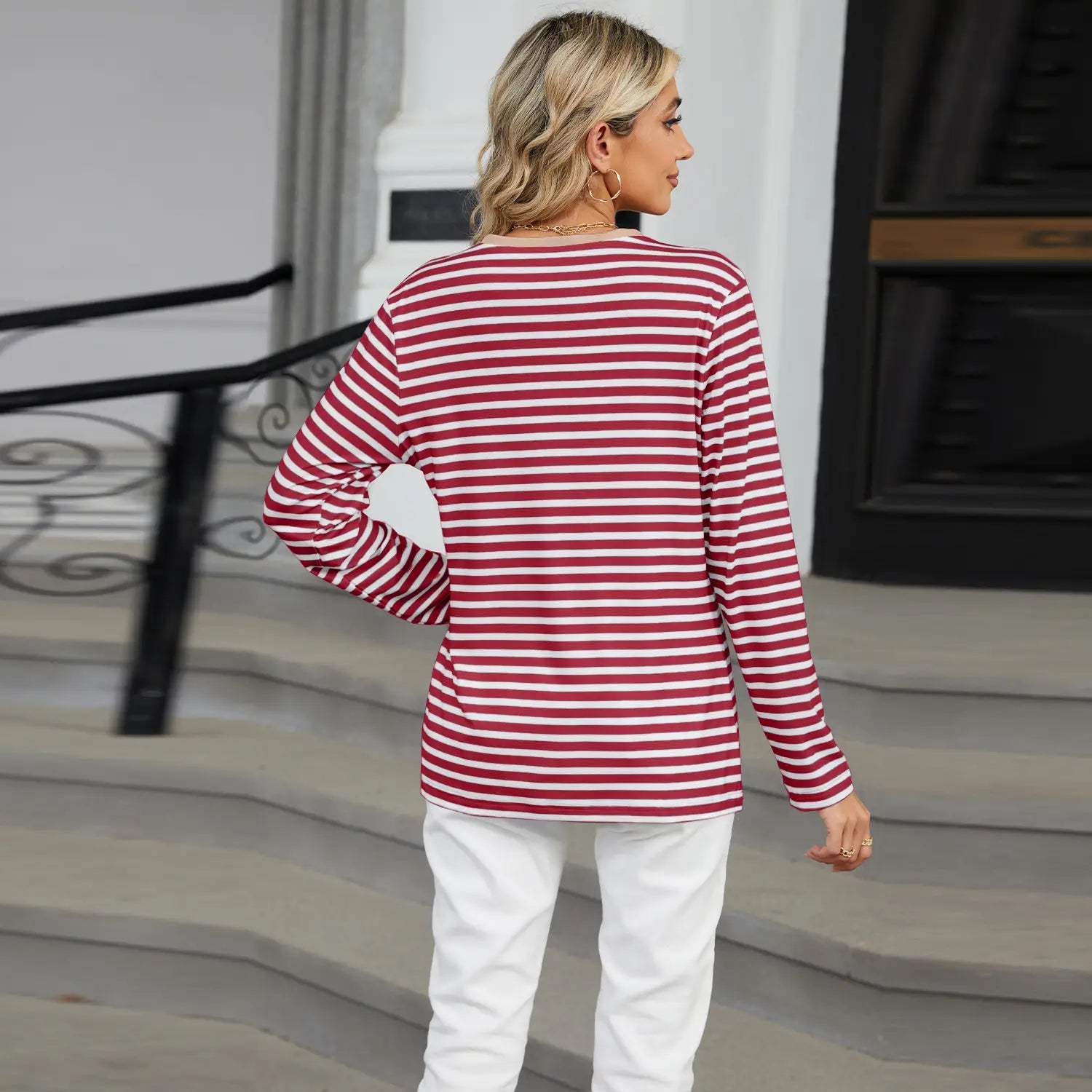 A woman wearing a striped contrast henley long sleeve v neck t shirt with red and white horizontal stripes.