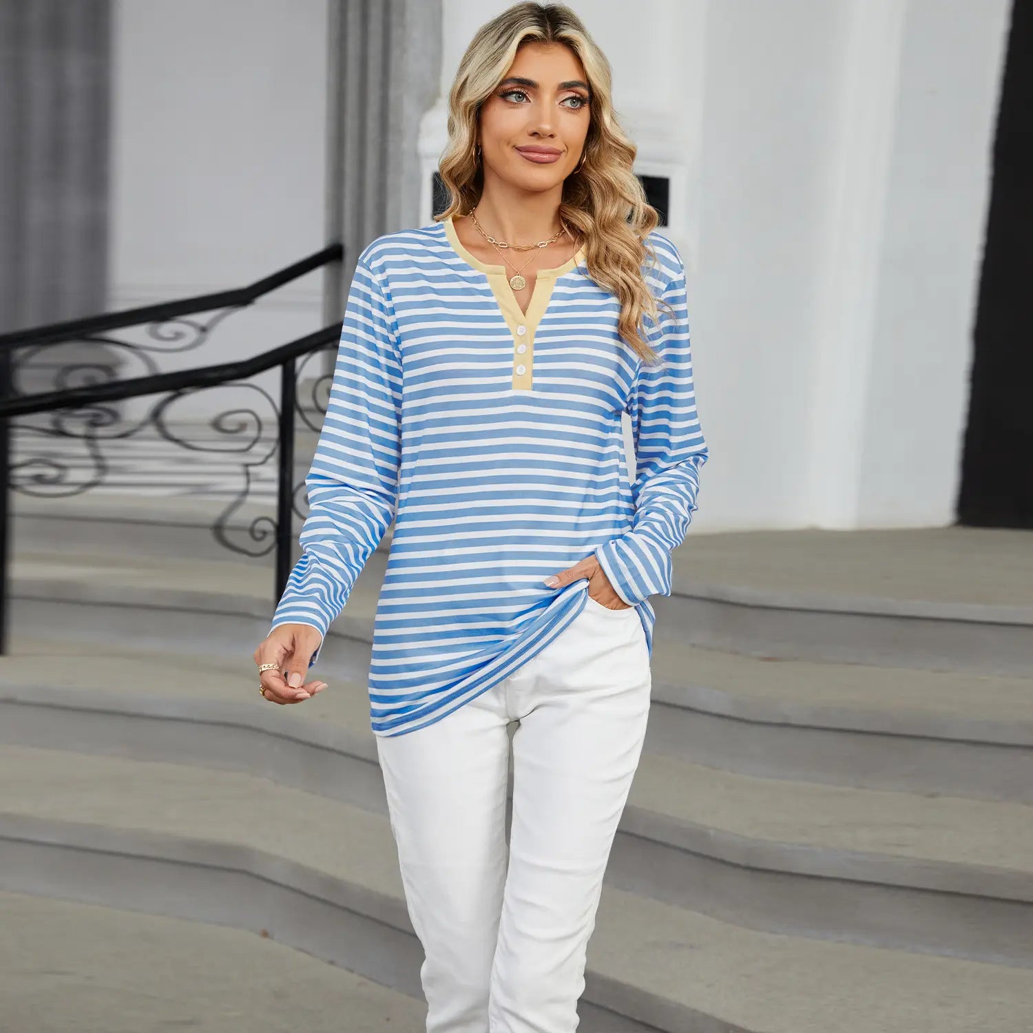 A woman wearing a striped contrast henley long sleeve v neck t shirt with long sleeves blue and white stripes and a yellow button front neckline.